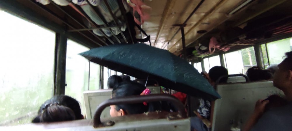 A passenger sits with an open umbrella to protect herself from the rain inside the NST operated Dimapur-Tening bus.